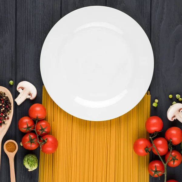 Sobre un fondo oscuro se encuentra un plato, pasta, tomates, especias — Foto de Stock