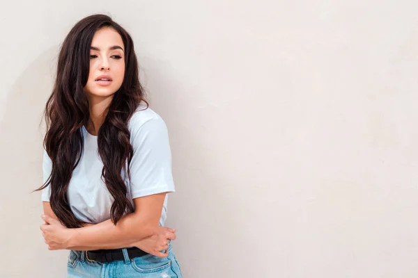 An alarmed girl grabbed her stomach, standing near a beige wall — Stok fotoğraf