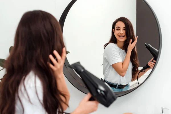 Mooi, speels brunette droogt haar haar en kijkt in de spiegel — Stockfoto