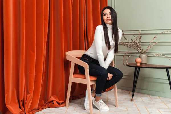Красивая, гламурная девушка сидит на стуле в студии на фоне красных занавесок — стоковое фото