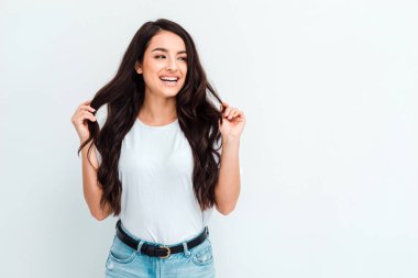 Young woman posing and smiling, straightening her hair over white background