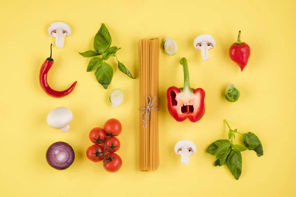 Concepto de cocina italiana. Sobre un fondo amarillo, un conjunto de ingredientes, pasta, tomates, pimientos, setas, albahaca — Foto de Stock