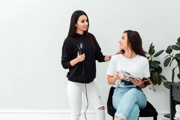 A professional, beautiful hairdresser holds a hair straightener and asks for client's wishes — 스톡 사진