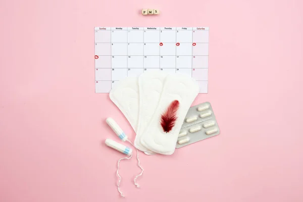 Tampon, feminine, sanitary pads for critical days, feminine calendar, pain pills during menstruation and a red feather on a pink background. Care of hygiene during menstruation. — Stock Photo, Image