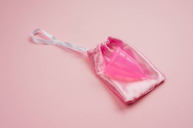  Menstrual  silicone cup lying on silk bag on pink background