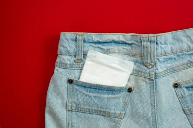 Woman pad in the pocket of female jeans on a red background. - I