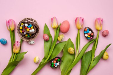 Multi-colored candy in the chocolate eggs and fresh tulips lie o