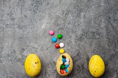 Multi-colored candies in the yellow egg  on a grey plaster backg