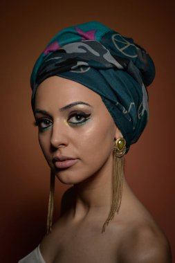 Sarık güzel kadın. Genç güzel kadın Türban ve altın aksesuarlar ile. Güzellik modaya uygun kadın Türban içinde sarılı tüyleri ile. Çok beyaz modeli Studio poz küpeler.