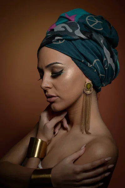 Mulher bonita em um turbante. Mulher bonita nova com turbante e acessórios dourados. Mulher elegante da beleza com cabelos envoltos em turbante. Modelo muito caucasiano usando brincos posando em estúdio . — Fotografia de Stock