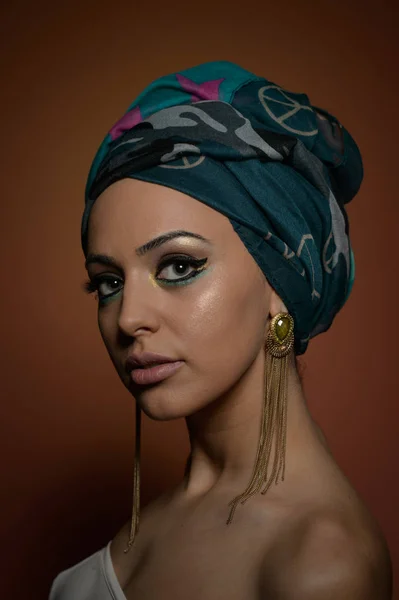 Mulher bonita em um turbante. Mulher bonita nova com turbante e acessórios dourados. Mulher elegante da beleza com cabelos envoltos em turbante. Modelo muito caucasiano usando brincos posando em estúdio . — Fotografia de Stock