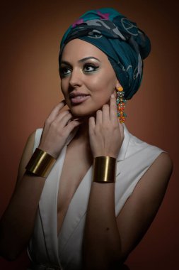 Türban ile güzel bir kadın. Türban ve altın aksesuarlar genç çekici kadın var. Saçlı güzellik modaya uygun kadın Türban içinde sarılı. Çok beyaz modeli Studio poz küpeler.