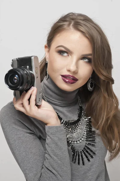 Blonde girl with camera looking forward. Beautiful blonde girl with black retro camera in studio against white wall.Sensual Woman taking photo on retro camera — Stock Photo, Image