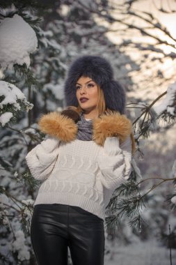 Ormandaki kış manzarası zevk aşırı büyüklükteki kürk kapaklı beyaz kazak güzel kadın. Sarışın kız karla kaplı ağaçların dalları altında poz. Çekici genç bayan parlak soğuk günde, makyaj