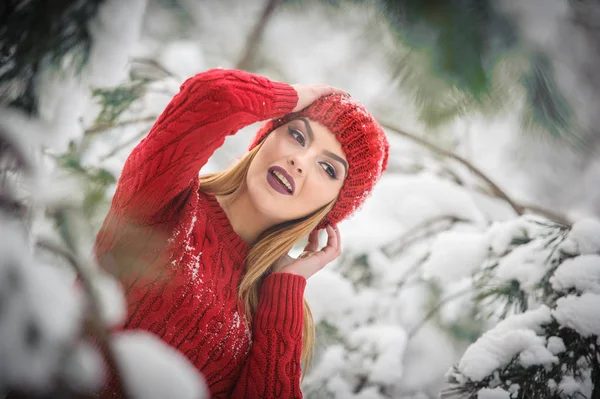 Bella donna in rosso con mantello di pelliccia marrone godendo il paesaggio invernale nella foresta. Ragazza bionda posa sotto rami di alberi innevati. Giovane femmina con fiocchi di neve intorno in giorno freddo lucente, trucco — Foto Stock