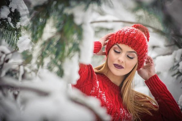 Mooie vrouw in het rood met bruin bont cape genieten van de winter landschap in bos. Blond meisje poseren onder besneeuwde bomen takken. Jonge vrouw met sneeuwvlokken rond in heldere koude dag, make-up — Stockfoto