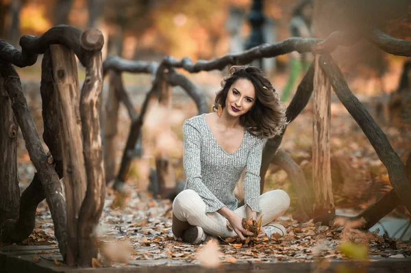 Fille sensuelle avec de longues jambes allongées dans une scène automnale.longues jambes blondes attrayant avec les cheveux bouclés relaxant dans le parc automnal. jeune femme à la mode posant dans la forêt . — Photo