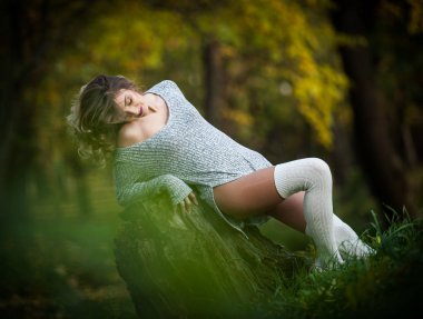 uzun bacakları güdük bir sonbahar sahne üzerinde oturan şehvetli kız. Uzun bacaklar çekici sarışın kıvırcık saçlı rahatlatıcı sonbahar Park. Ormandaki bir güdük poz şık genç kadın.