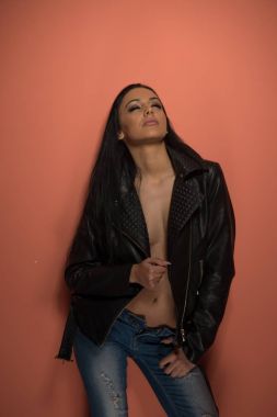 Çekici seksi esmer siyah deri ceket ve kot kışkırtıcı kapalı poz. Şehvetli kadın iç çamaşırı, atış stüdyo olmadan uzun siyah saçlı portresi. Çekici genç bayan cazip