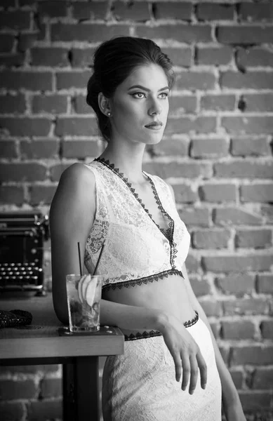 Belle dame à la mode avec robe blanche debout près d'une table de restaurant prendre un verre. Femme brune cheveux courts avec maquillage et coupe de cheveux créative tenant un verre avec frais — Photo