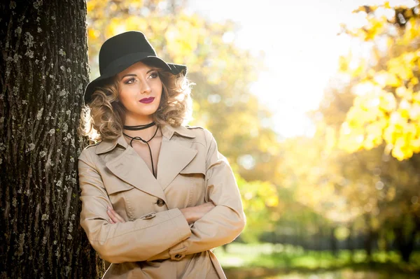 Belle femme blonde avec manteau crème, longues jambes et chapeau noir dans une scène d'automne.Portrait d'une très belle jeune femme élégante et sensuelle aux cheveux bouclés posant dans le parc d'automne . — Photo