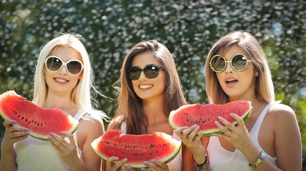 Hermosas chicas con gafas de sol comiendo sandía fresca y sonrisas.Feliz joven mujer comiendo sandía en el parque. Estilo de vida juvenil. Felicidad, alegría, concepto de verano . — Foto de Stock