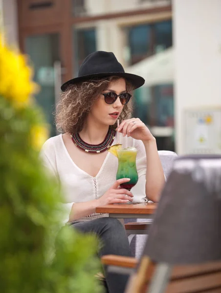 Happy Brunette Girl with sunglasses Sitting at the Park, Drinking a glass of Cold Green Juice While Smiling Into the Distance. Young pretty woman on the bench  drinking  juice wearing a white shirt — Stock Photo, Image