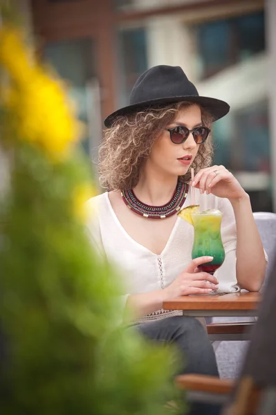 Happy Brunette Girl with sunglasses Sitting at the Park, Drinking a glass of Cold Green Juice While Smiling Into the Distance. Young pretty woman on the bench  drinking  juice wearing a white shirt — Stock Photo, Image