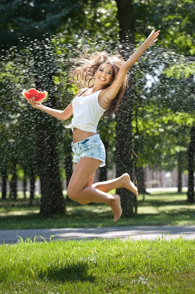 Portrait of young sexy woman in spray of water with watermelon.She has a good gentle skin, her hair flying, and she smiles.Happy young woman  in park. Youth lifestyle. Happiness, joy, summer concept. — Stock Photo, Image