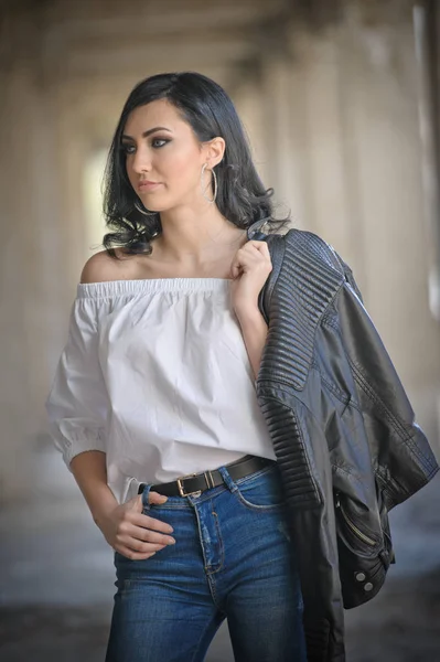 Retrato de hermosa joven sexy con traje negro, chaqueta de cuero sobre lencería, en fondo urbano. Atractiva morena con piernas largas perfectas en tacones altos sandalias de plata posando de moda . —  Fotos de Stock