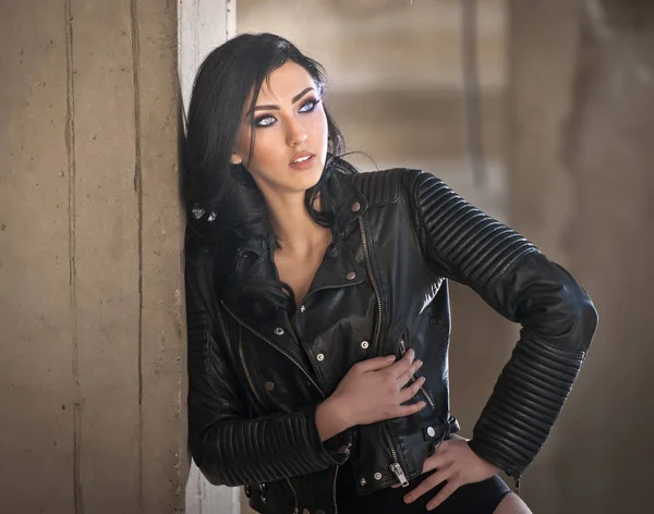 Retrato de hermosa joven sexy con traje negro, chaqueta de cuero sobre lencería, en fondo urbano. Atractiva morena con piernas largas perfectas en tacones altos sandalias de plata posando de moda . — Foto de Stock