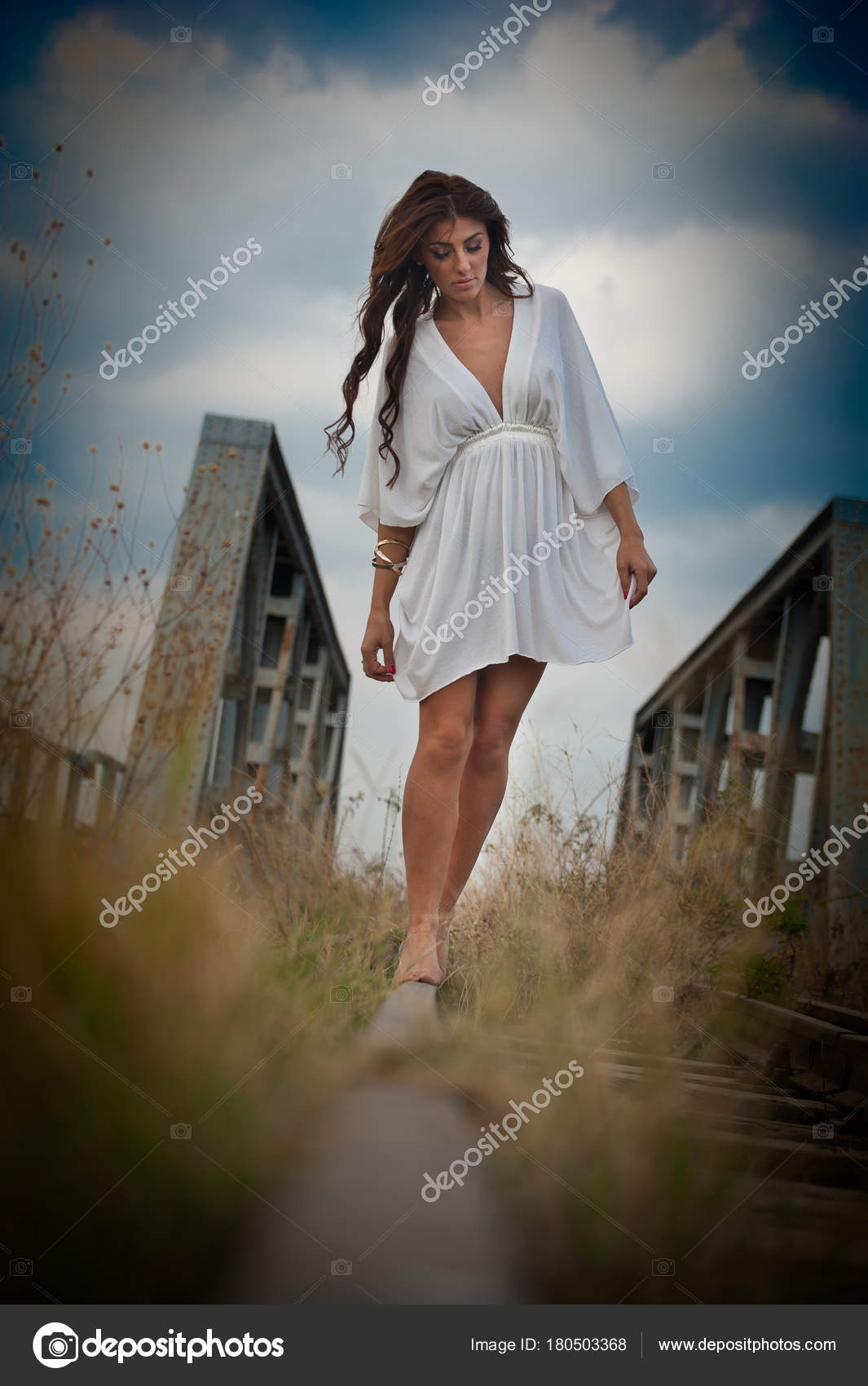 Attraktiv kort hvid kjole og langt hår stående på skinnerne med bro i baggrunden. Fashion sexet pige med sexet krop og lange ben på broen forklædt i hvid kjole —