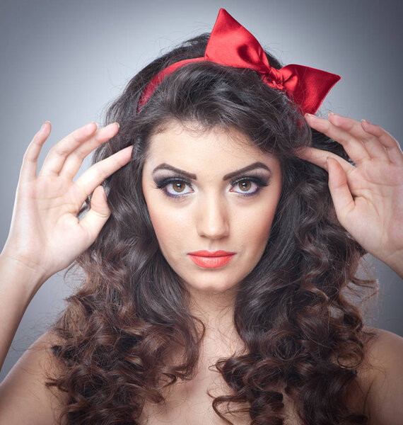 Девушка с красным бантом на голове и красным бюстгальтером посылает поцелуи модели на сером заднем плане.
