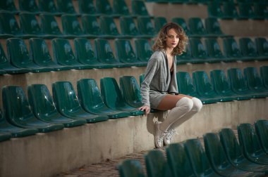 bir alanın mahkemelerde uzun bacaklar ile şehvetli kız. Uzun bacaklar çekici sarışın kıvırcık saçlı tribünlerde sandalyeye rahatlatıcı. Şık genç kadın ile beyaz yün külotlu şehvetli poz