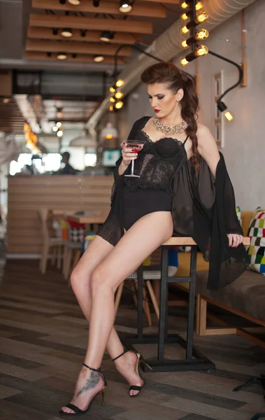 長い足と高いヒールを持つ官能的な女の子はバーの飲酒で椅子に座っています 屋内シーンで美しい体と高いヒールを身に着けているハンサムな女の子 長いセクシーな足を持つファッションモデルはカクテルを飲みます — ストック写真