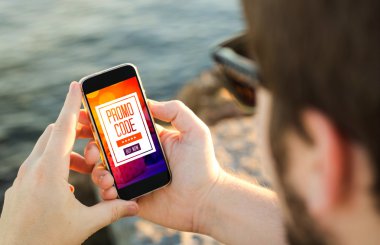 sahilde adam telefonunu tutarak ve bir promosyon kodu kullanarak