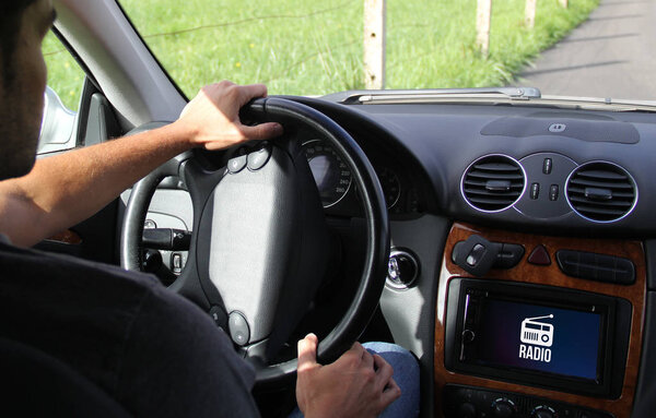 young man driving a connected car showing radio on the onboard computer
