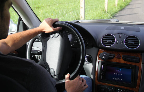young man driving a connected car showing music on the onboard computer
