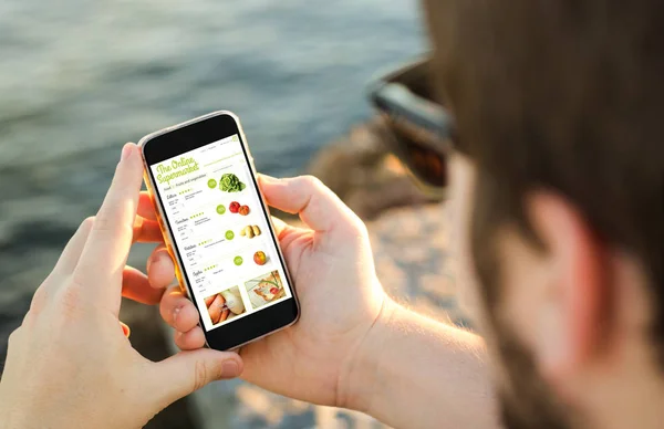 Мужчина, покупающий продукты онлайн со своего мобильного телефона на побережье — стоковое фото