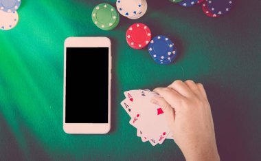 boş ekran, cips ve kartların üzerinde yeşil poker masası, kartları tutan erkek el ile akıllı telefon. Kumar kavramı