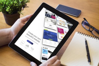 Web sitesi oluşturucu ahşap çalışma masa üzerinde gösterilen tablet tutan adamın elleri.
