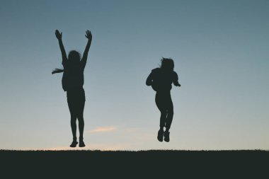 Küçük kız siluet günbatımında atlama. 