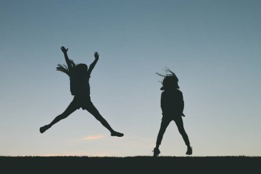 Küçük kız siluet günbatımında atlama. 