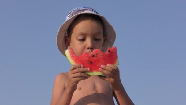 Happy boy appetizing eating red watermelon and juice flowing under the teeth. Video on the beach. 4K — Stock Video