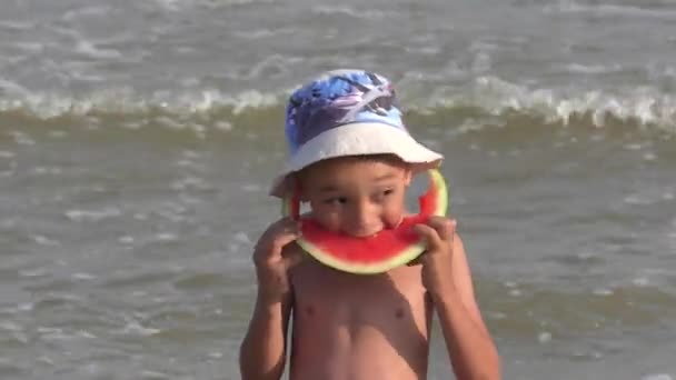 Happy boy smakelijk eten rode watermeloen en sap stroomt onder de tanden. Video op het strand. 4K — Stockvideo