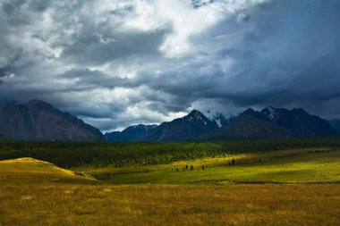 Güzel görünüm kar dağlar ve güneş ışığı ve fırtına gökyüzü ile yeşil alan