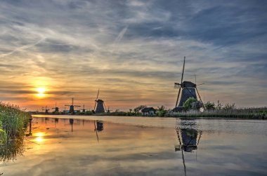 Cirrus bulutlar bir gökyüzü güneş ayarında ve doğal UNESCO Dünya Miras Listesi adlı bir kanal sakin suda birkaç yel değirmenleri ile birlikte yansıtan