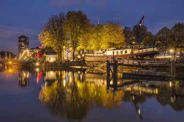 Rotterdam, Hollanda, 13 Kasım 2019: Sonbahar renklerinde eski tersane ve ağaçlar Eski Liman 'ın mavi saatindeki ayna benzeri suyunda yansıyor