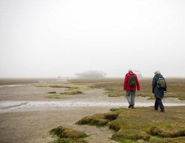 Sis kumsalda deniz üzerinde yürüyen insanlar 
