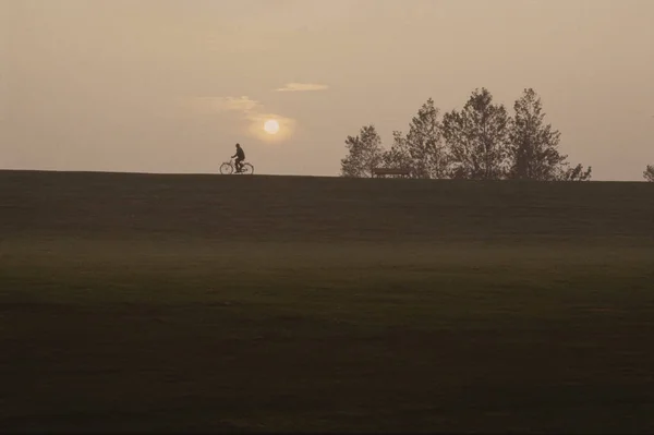 照片的人骑自行车在草地上日落时间 — 图库照片